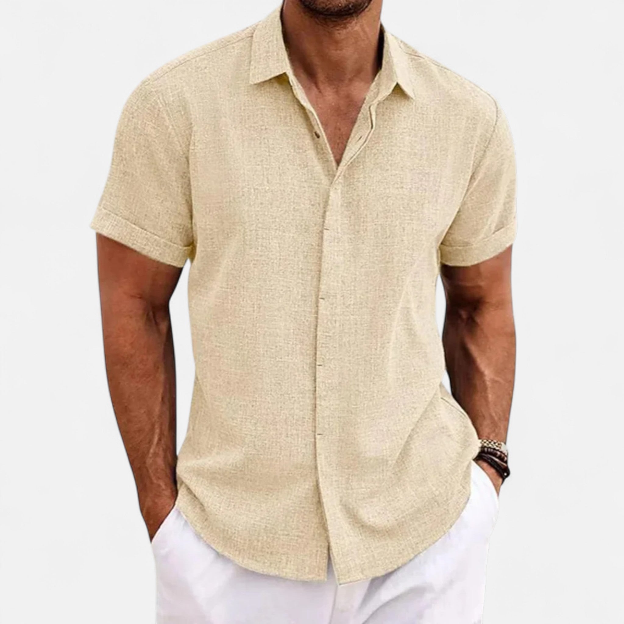 Man wearing a beige short-sleeve shirt and white pants on a light gray background