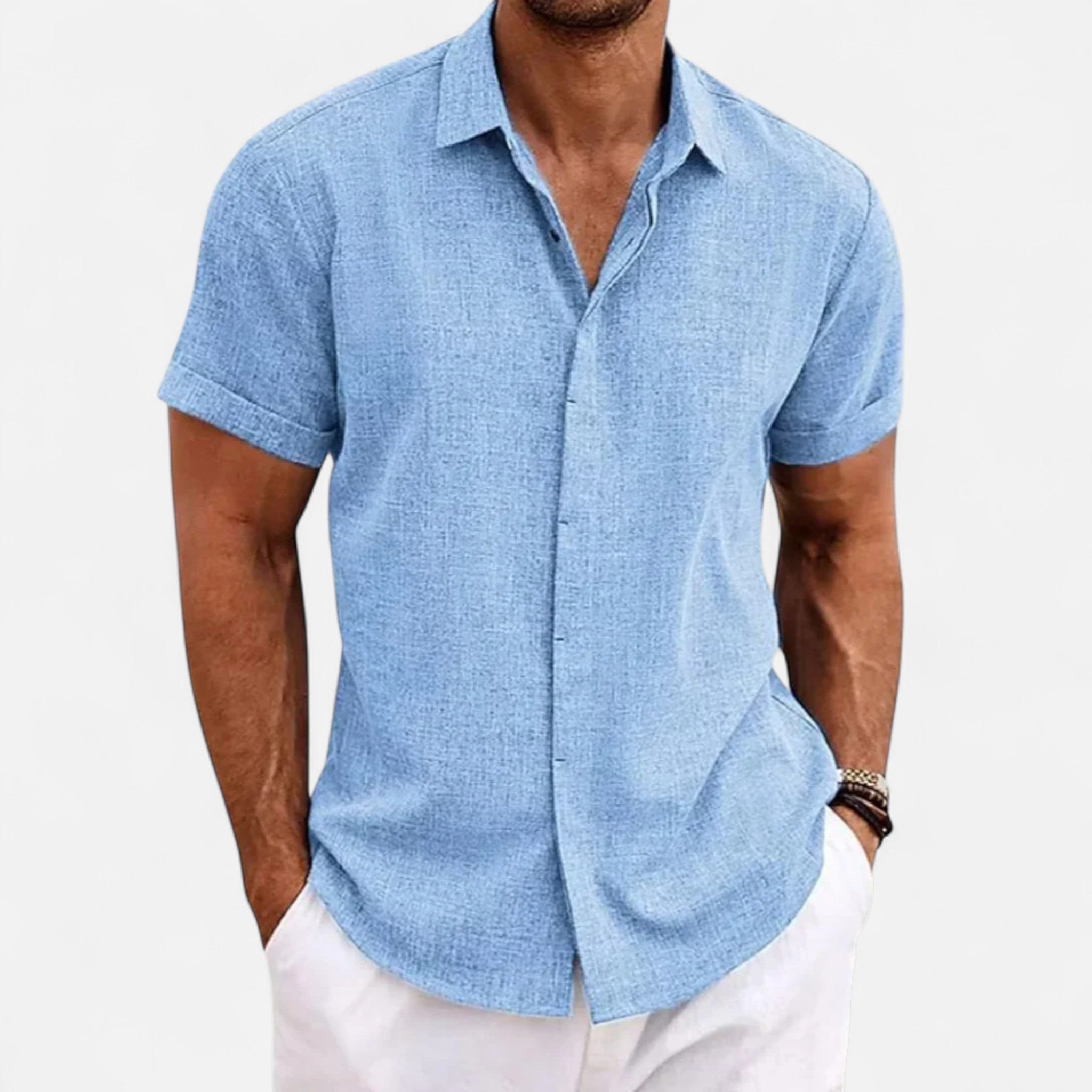 Man wearing a light blue short-sleeve shirt and white pants on a plain background