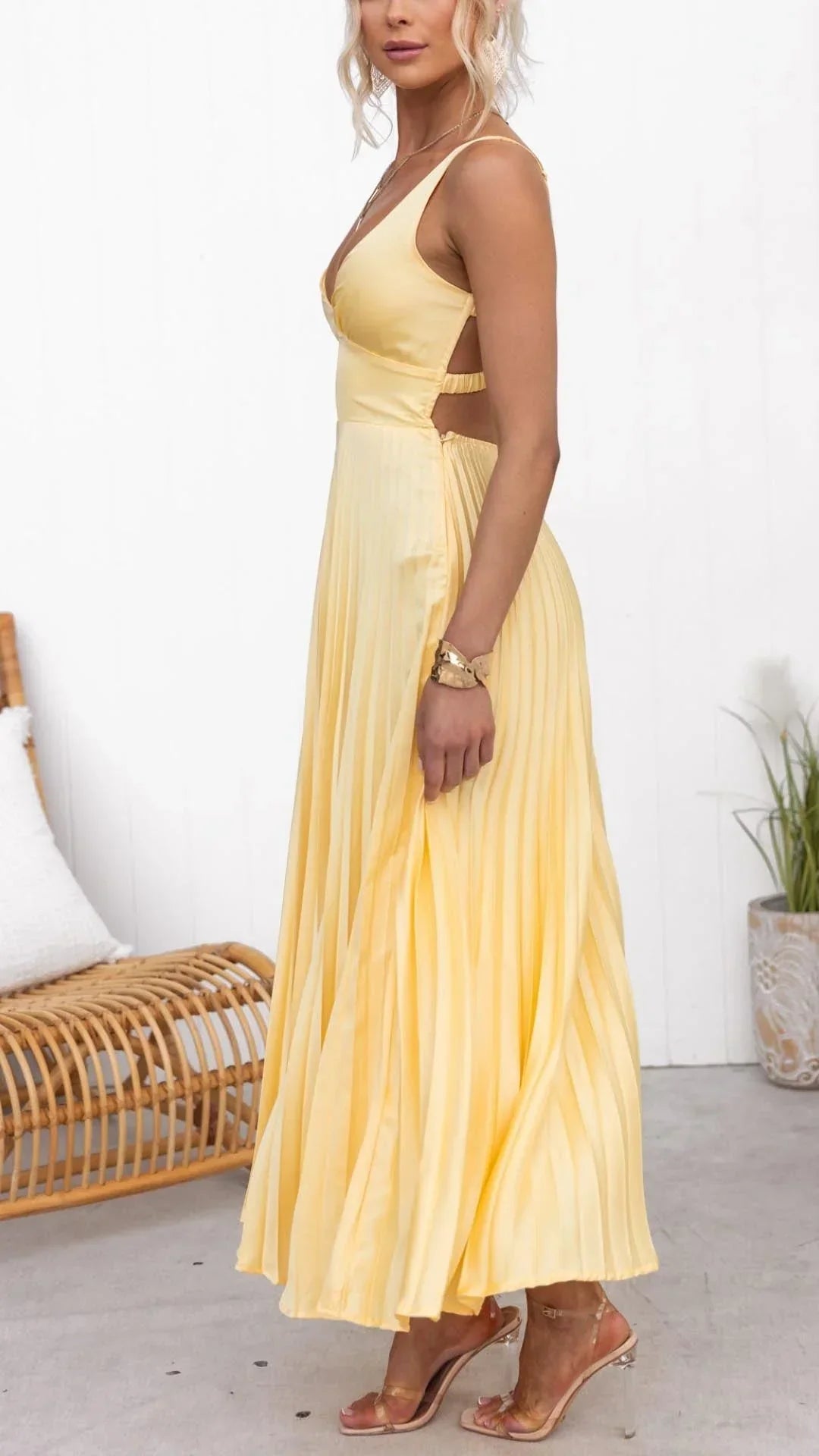 Woman wearing a yellow dress standing in a minimalistic room with a white wall and wooden chair.
