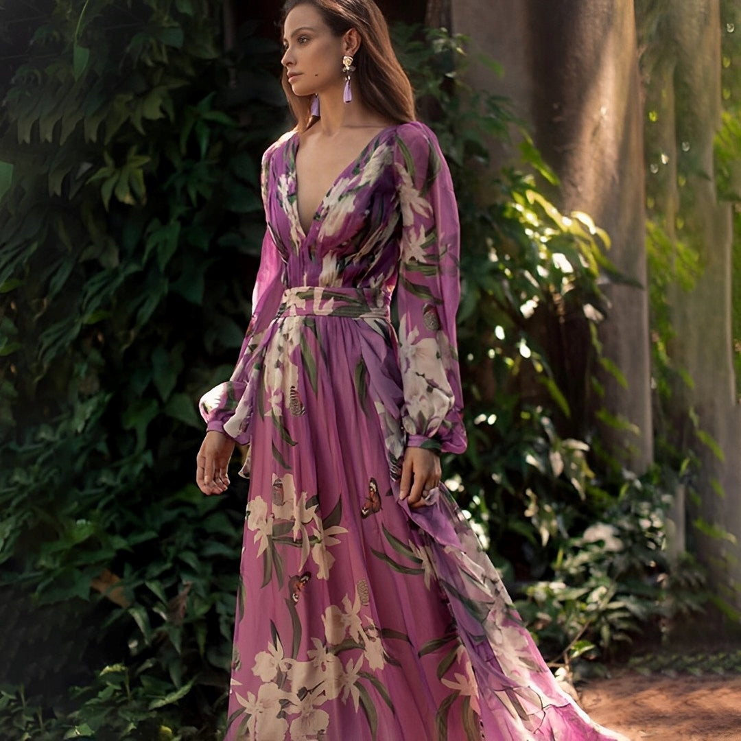 Woman in a purple floral dress standing in a natural setting with greenery.
