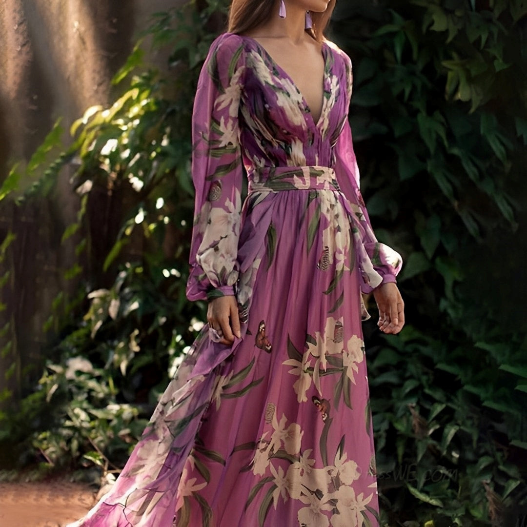 Woman wearing a long, floral-patterned dress with a blurred green foliage background