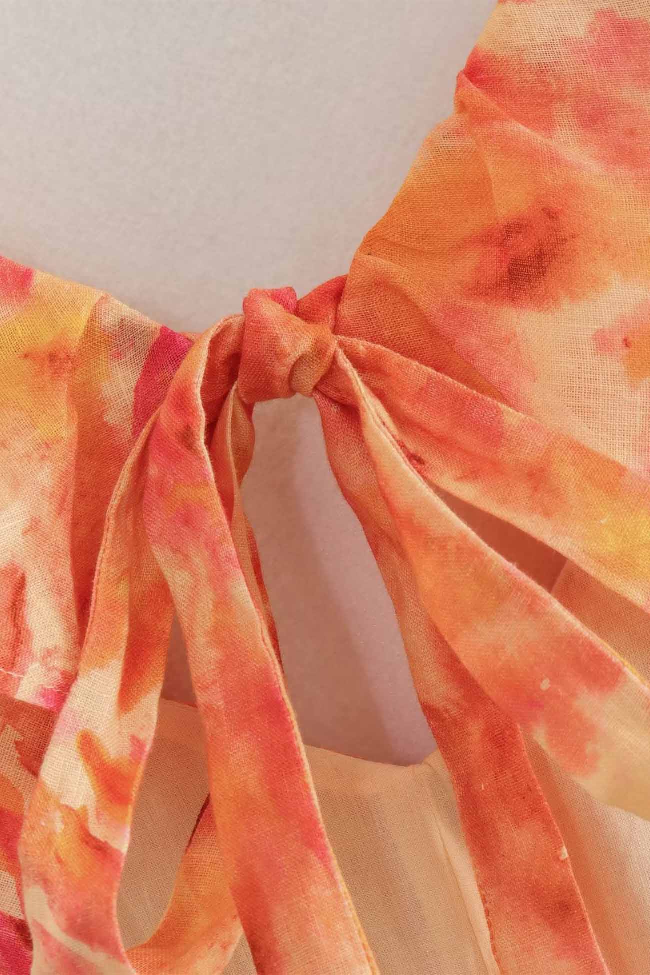Close-up of a tie-dye top with orange and yellow hues on a plain background