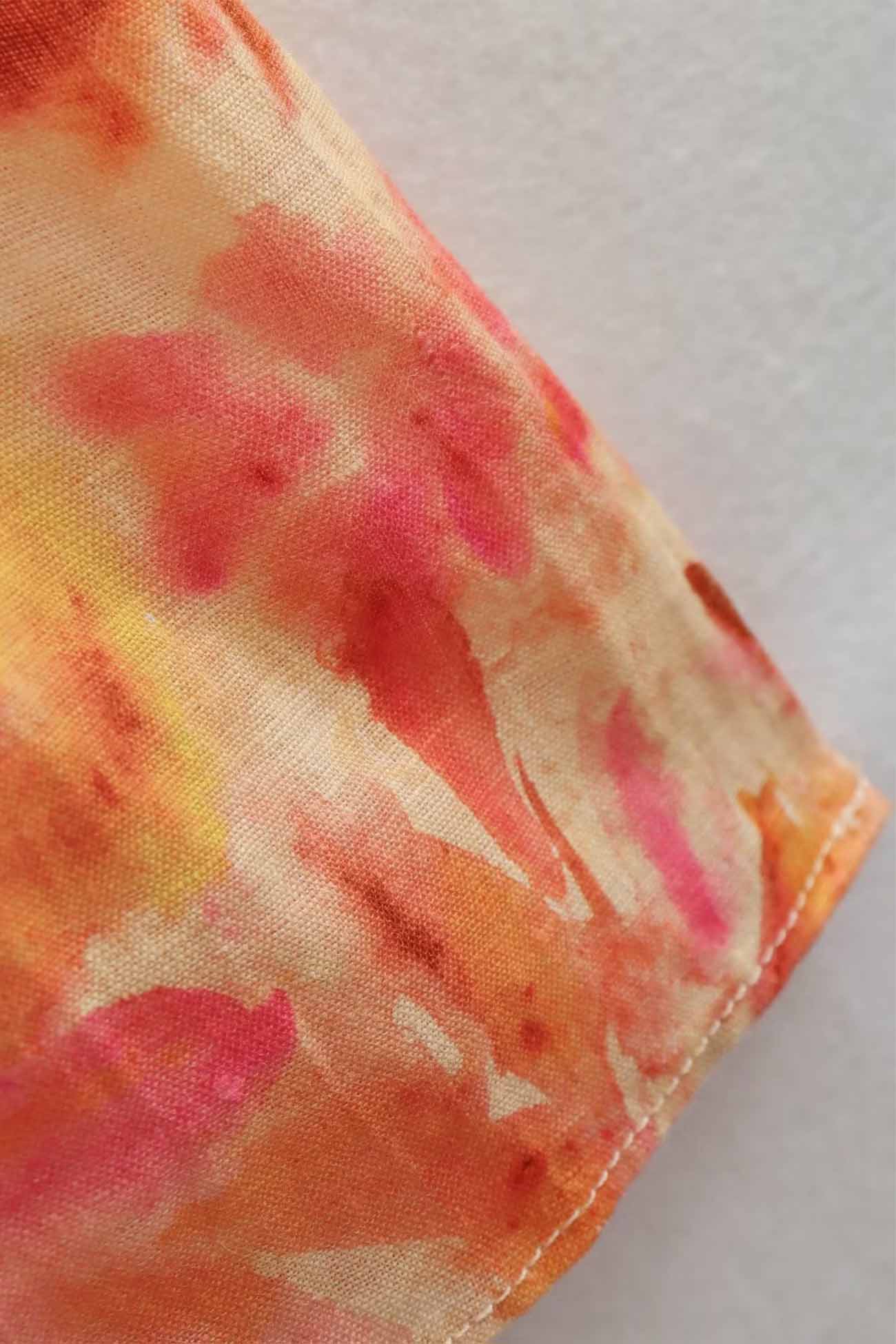 Close-up of a fabric with pink and orange tie-dye pattern on a white background