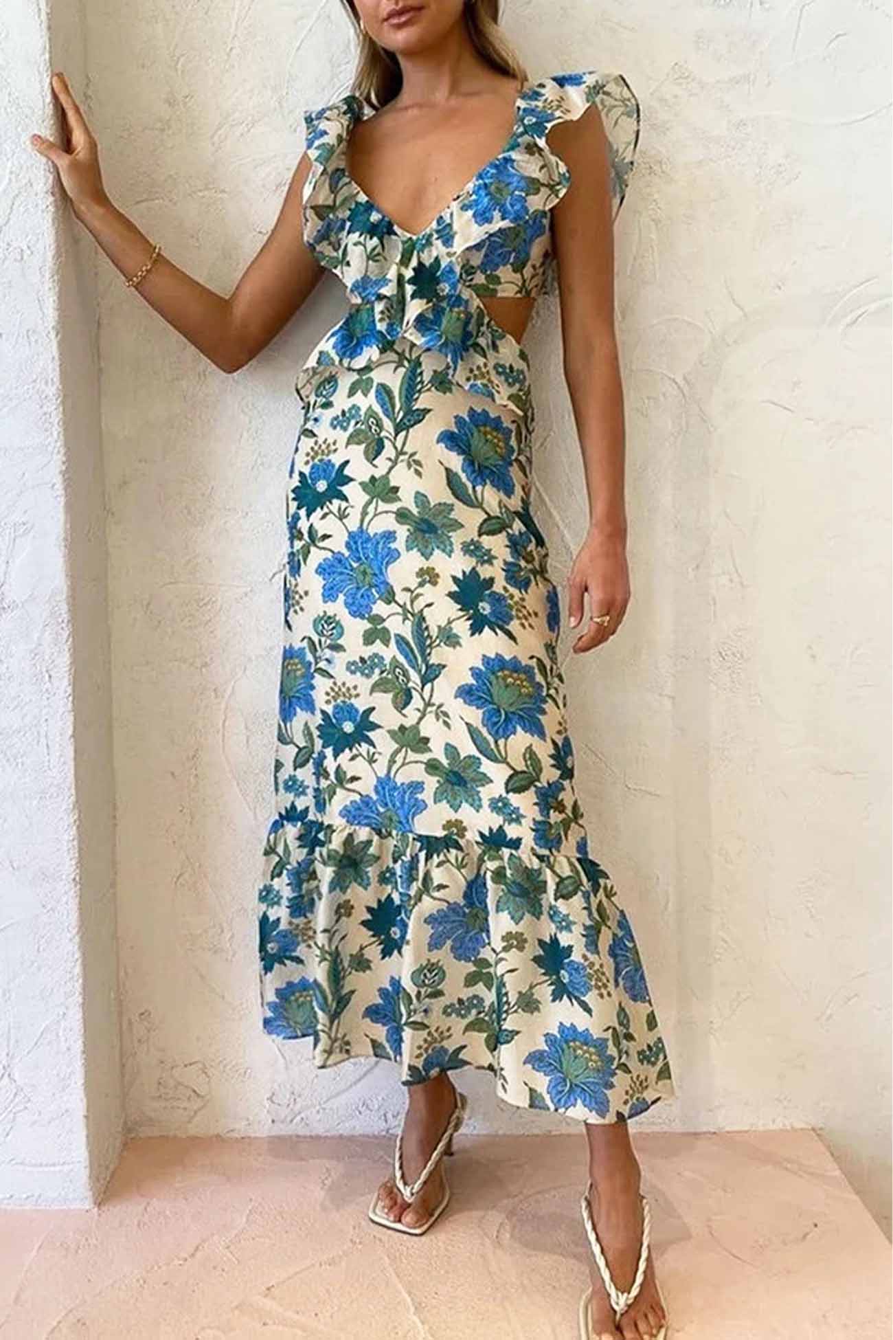 Woman wearing a floral dress with blue flowers against a white wall.