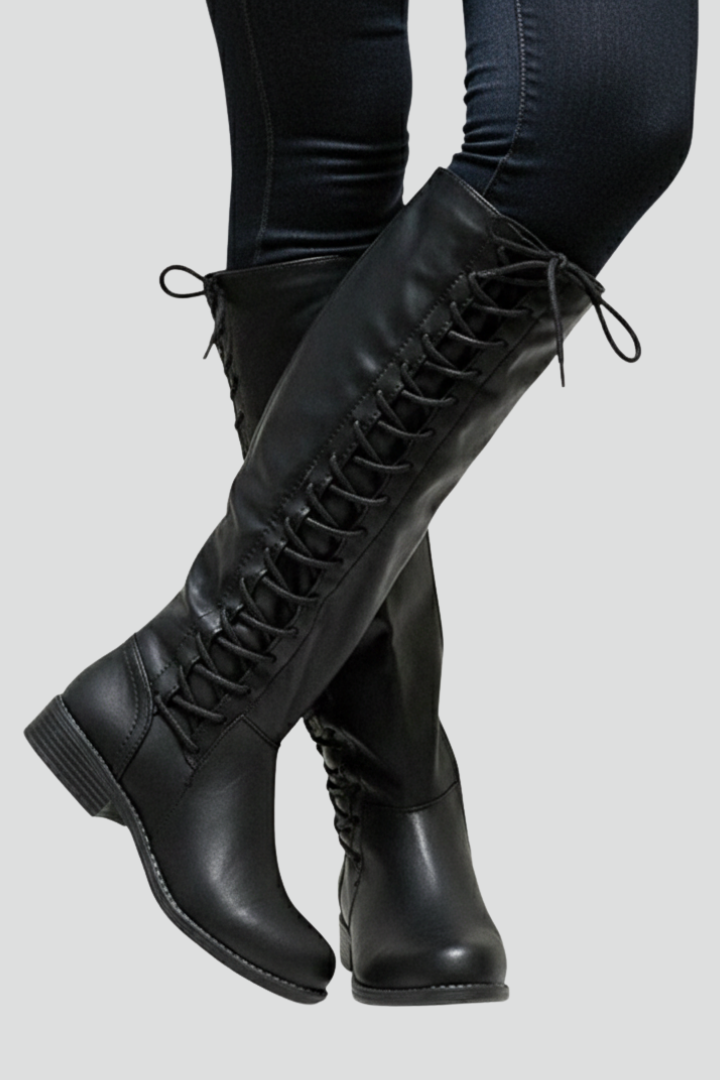 Black knee-high boots worn with black pants on a light gray background