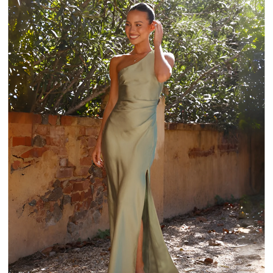 Woman in a green evening gown standing outdoors with a rustic wall and trees in the background