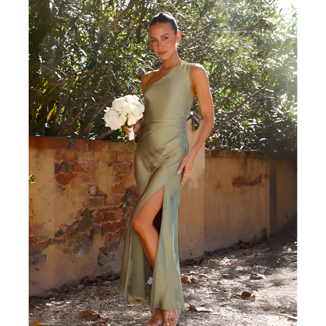 Woman in a green dress holding flowers against a rustic wall and tree background