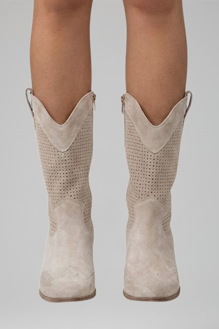 Beige cowboy boots worn by a person on a plain background