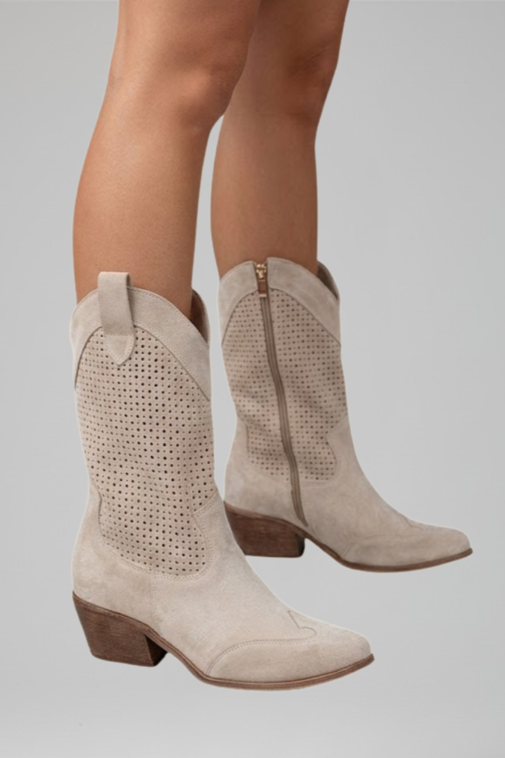 Beige suede cowboy boots with perforated design on a gray background