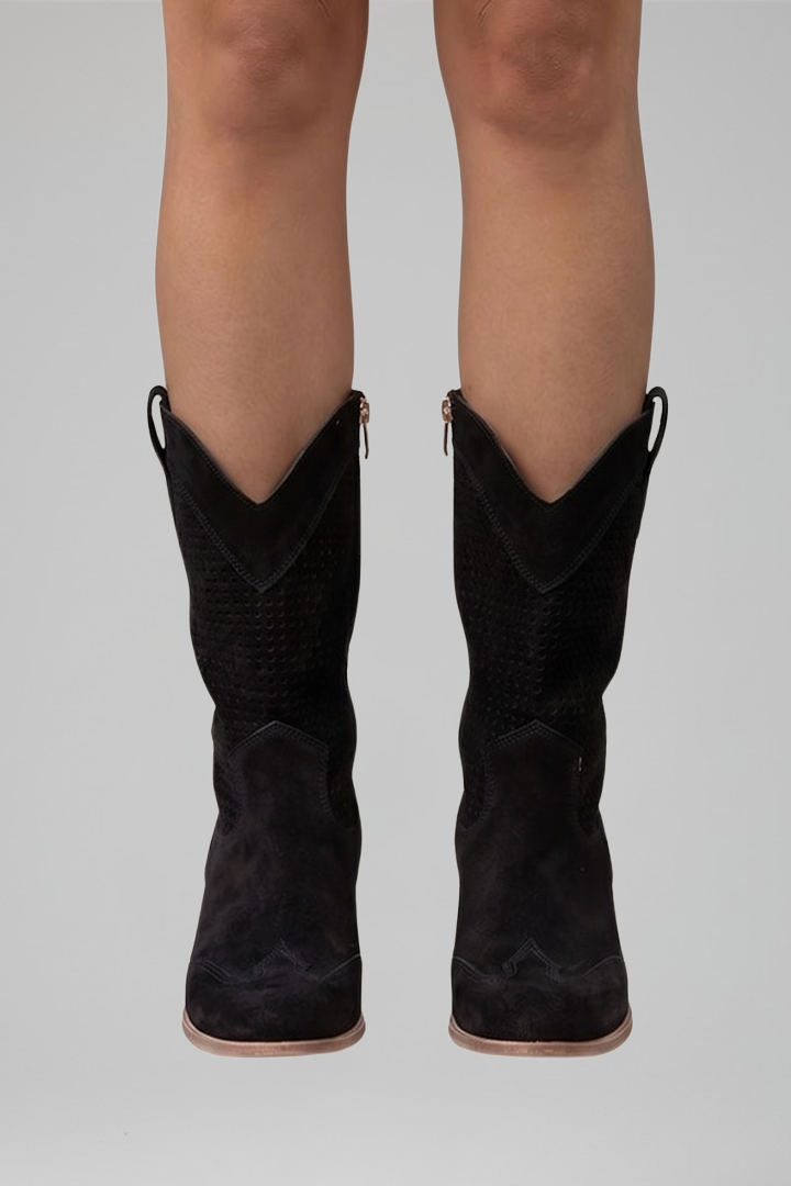 Black cowboy boots worn by a person on a gray background