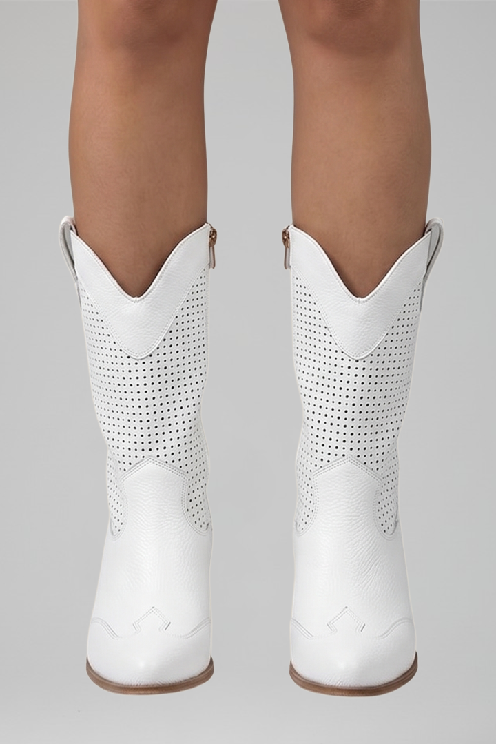 White cowboy boots with perforated design worn by a person on a gray background