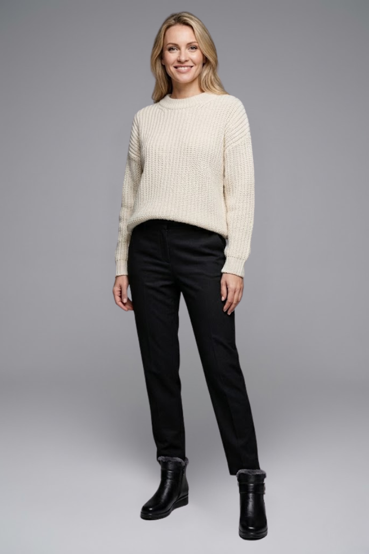 Woman wearing a cream sweater, black pants, and black boots on a gray background