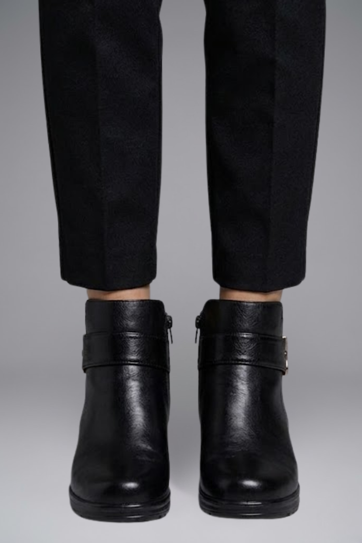 Black leather boots worn with black pants on a gray background