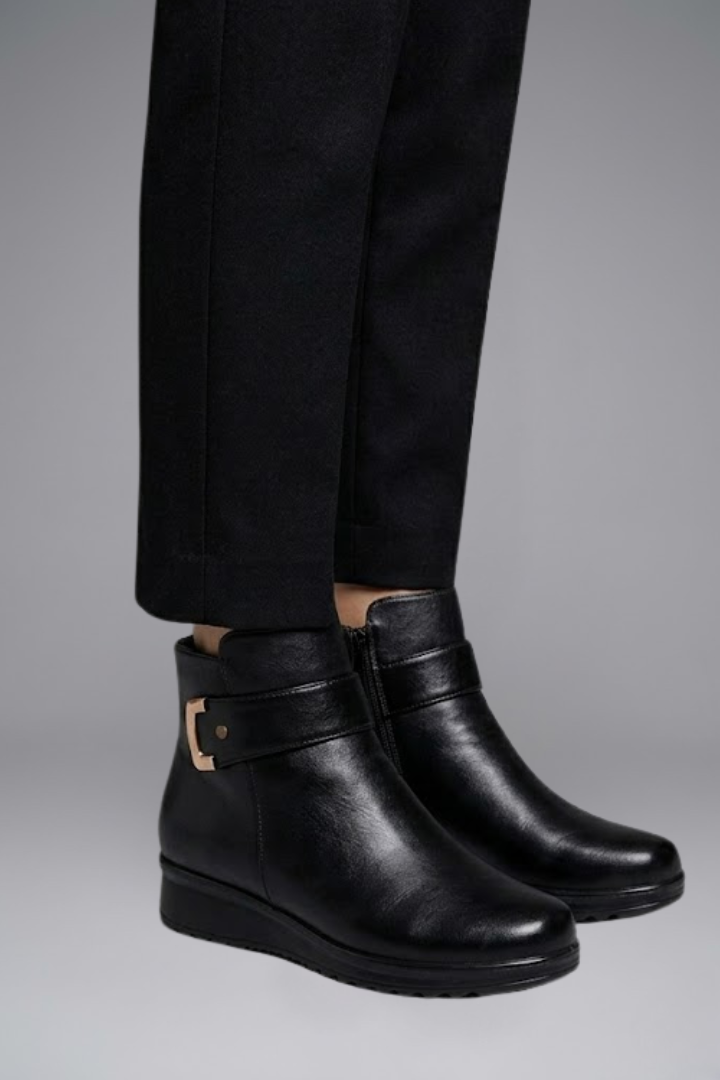 Black leather boots worn with black pants on a gray background