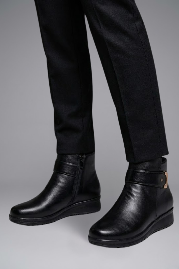 Black leather boots worn with black pants on a gray background