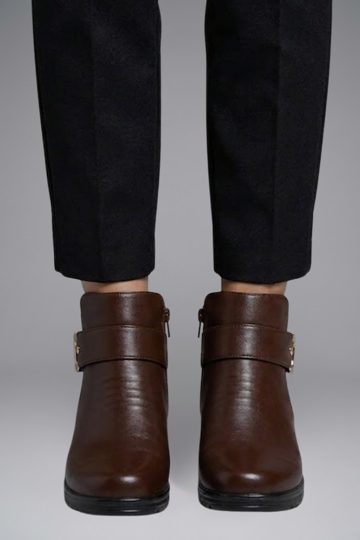 Brown leather boots worn with black pants on a neutral background