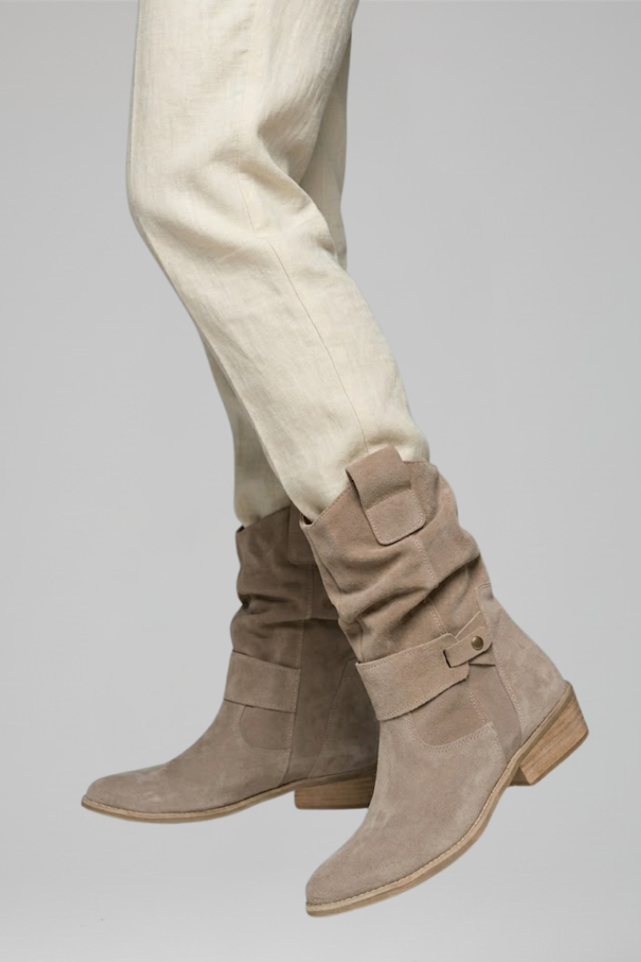Beige suede boots worn with beige pants on a light gray background