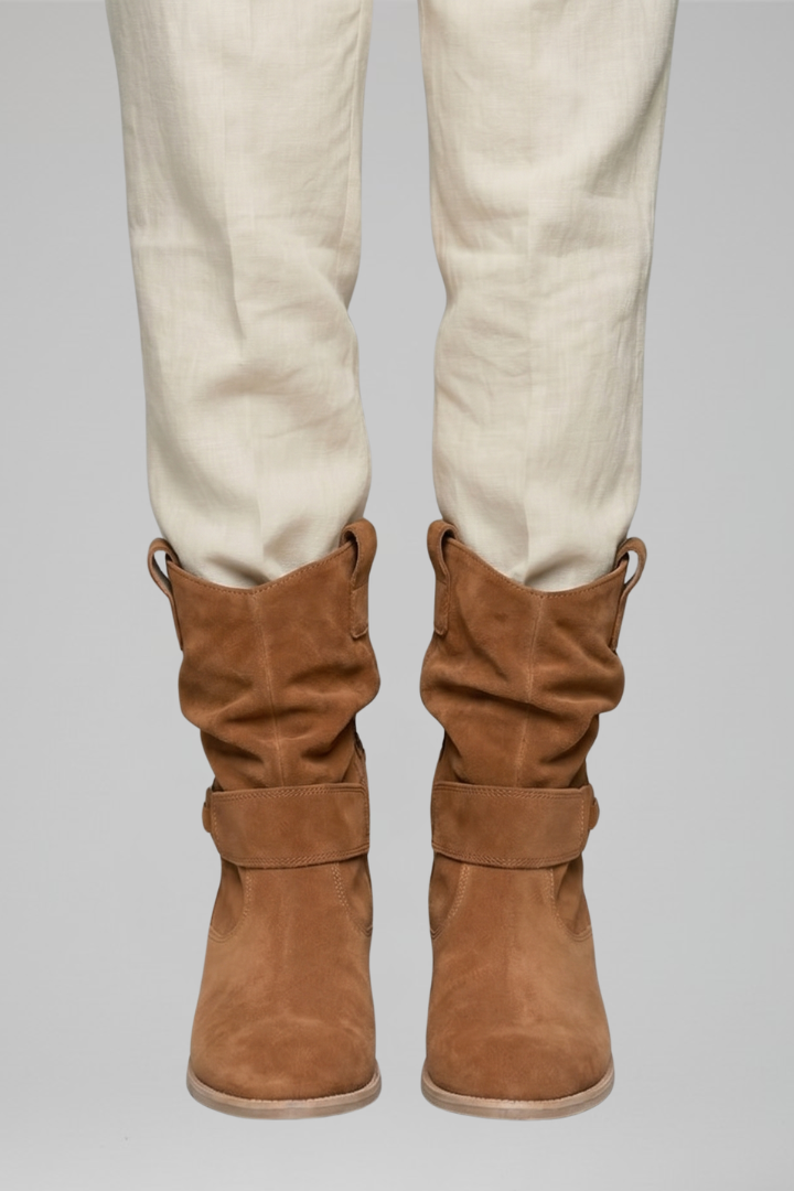 Brown knee-high boots worn with white pants on a gray background