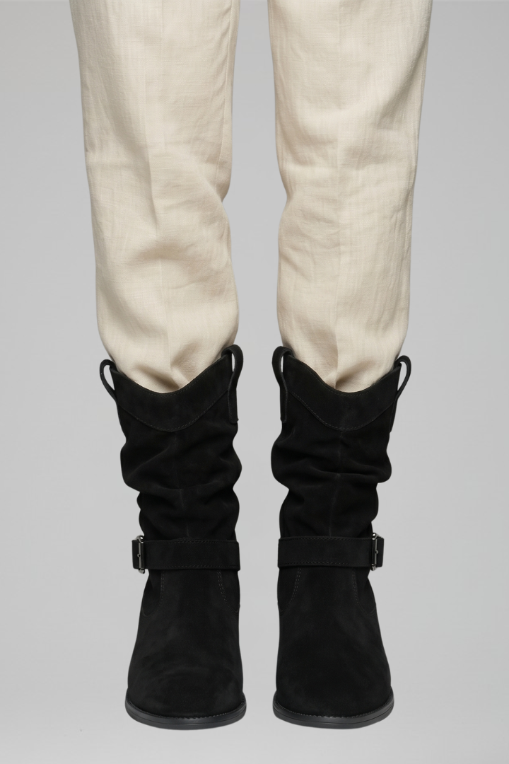 Black knee-high boots worn with beige pants on a gray background