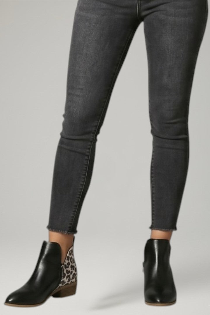 Person wearing black ankle boots with leopard print sole and gray jeans on a light gray background