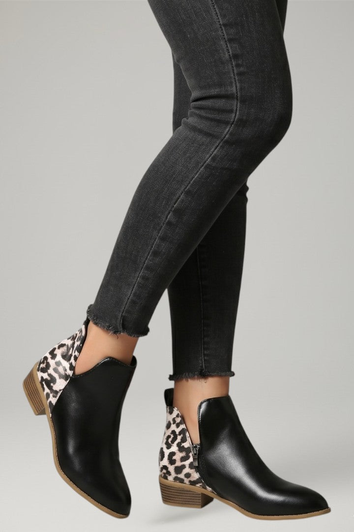 Black ankle boots with leopard print soles worn with black jeans on a gray background