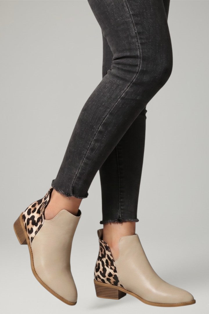 Beige ankle boots with leopard print details worn with black jeans on a light gray background