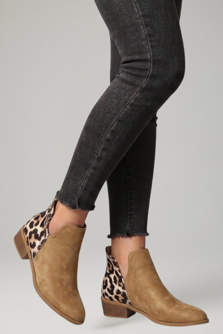 Brown ankle boots with leopard print details worn with black jeans on a gray background