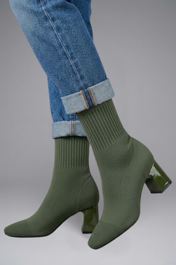 Green sock boots worn with rolled-up blue jeans on a gray background