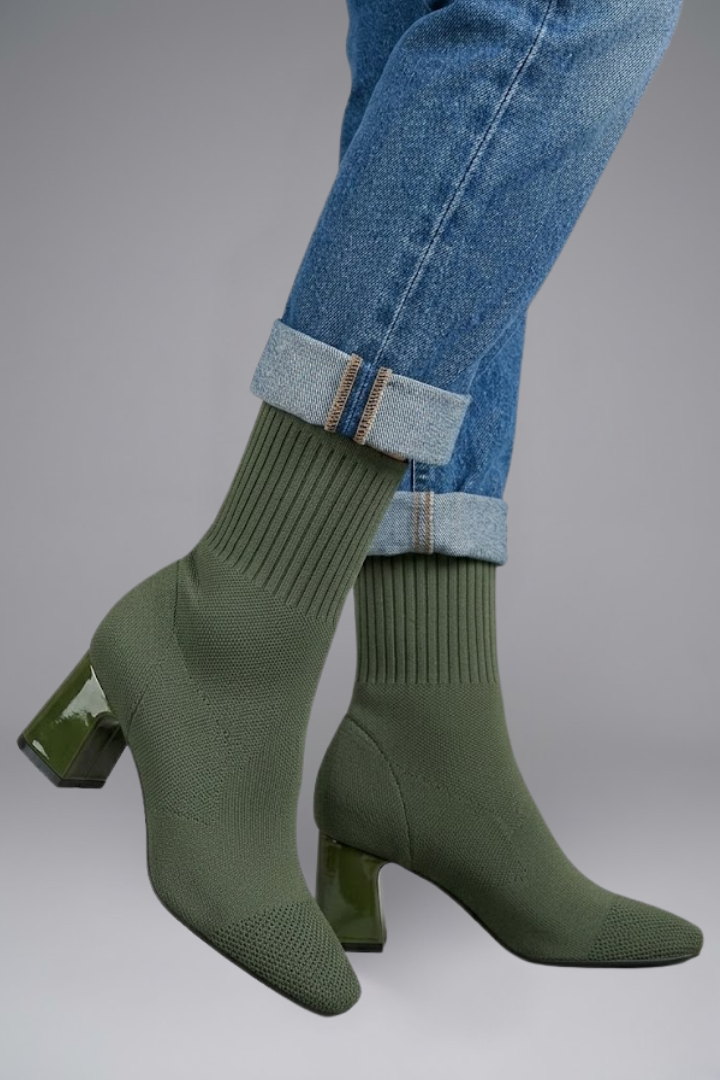 Green sock boots worn with rolled-up blue jeans on a gray background