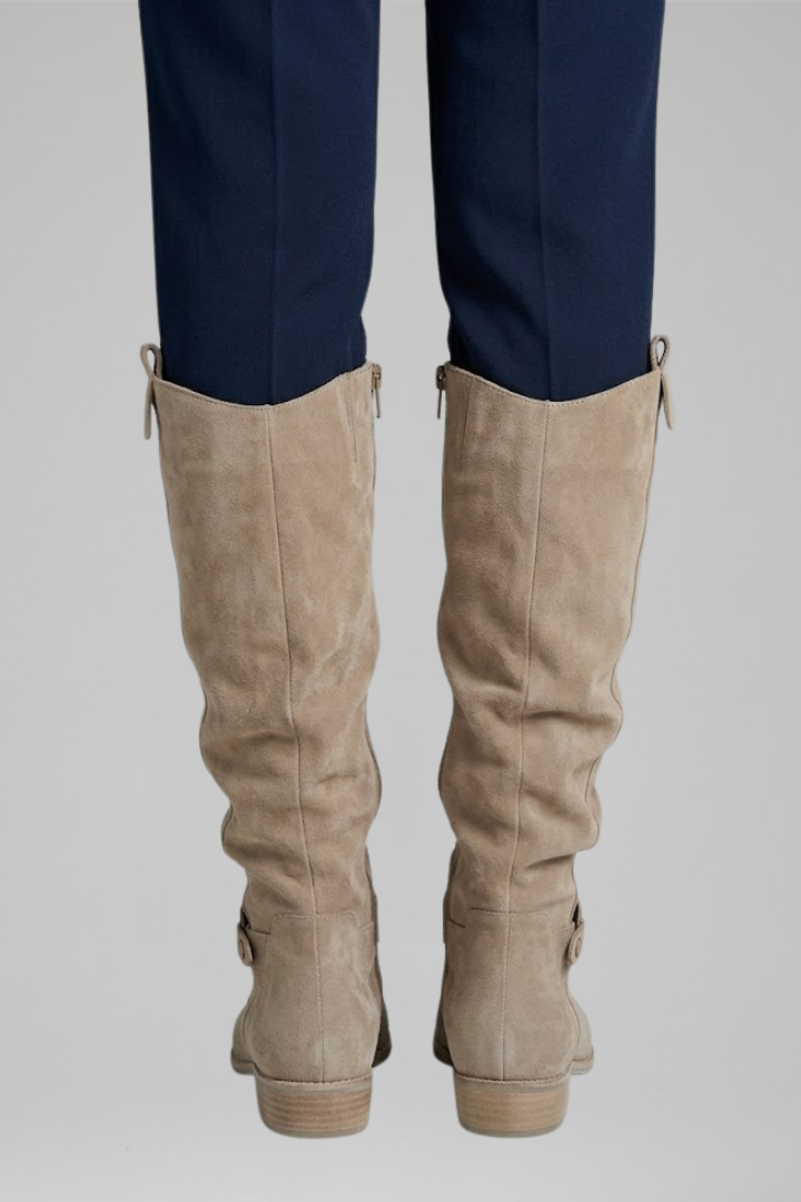 Beige knee-high boots worn with navy pants on a light gray background