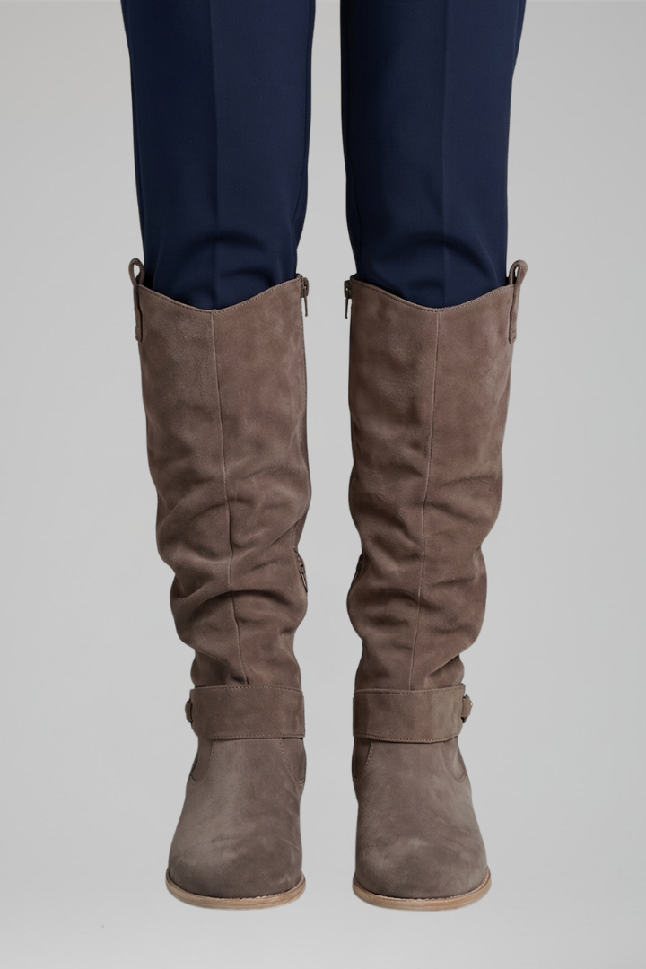 Brown knee-high boots worn with navy pants on a light gray background