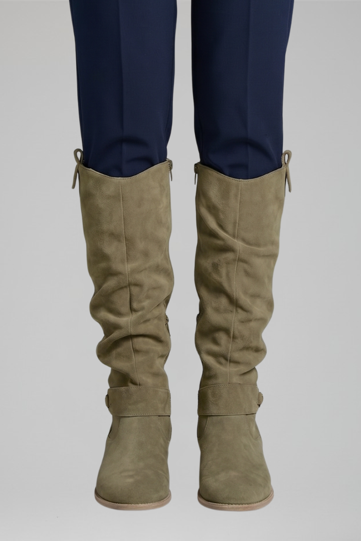 Green knee-high boots worn with navy pants on a plain background