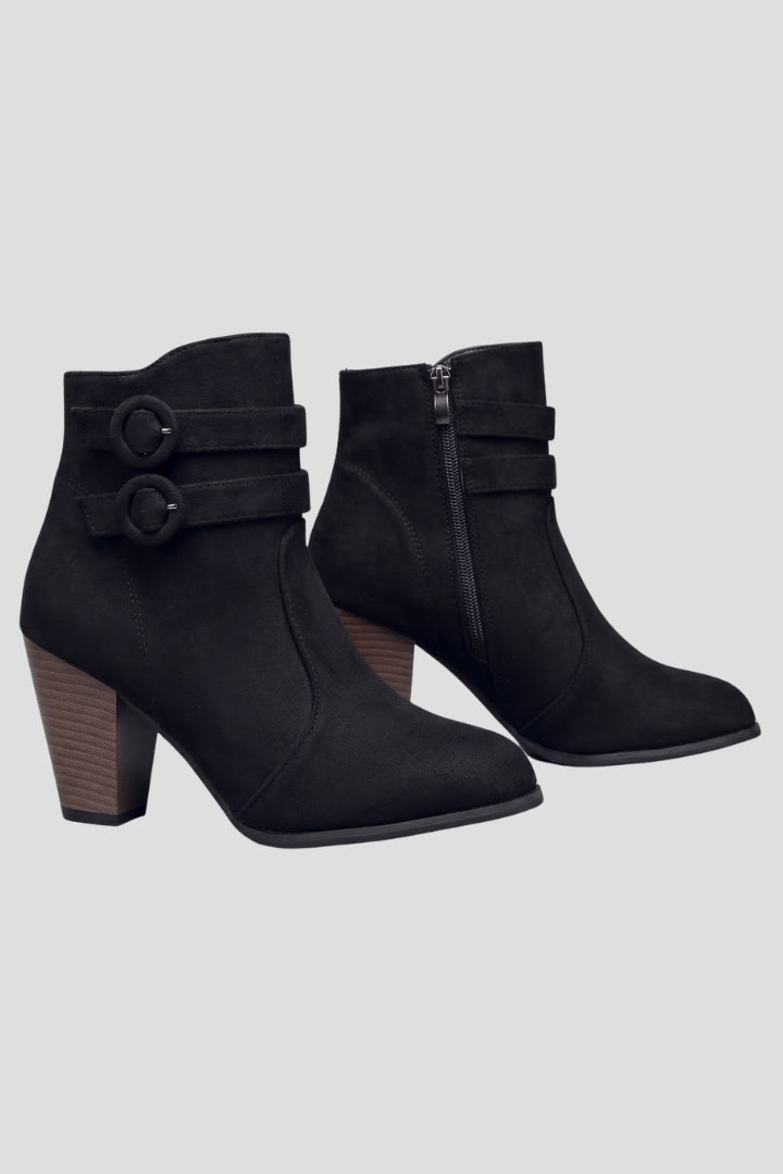 Black ankle boots with decorative straps on a light gray background