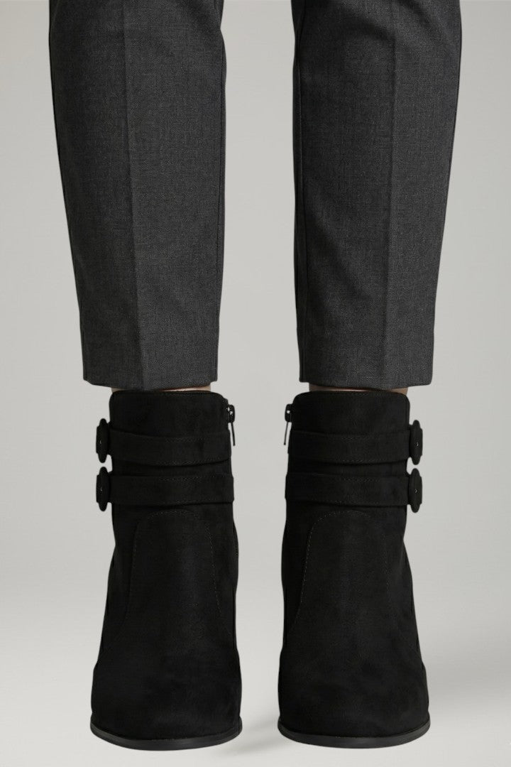 Black suede boots with buckles worn with gray pants on a light gray background