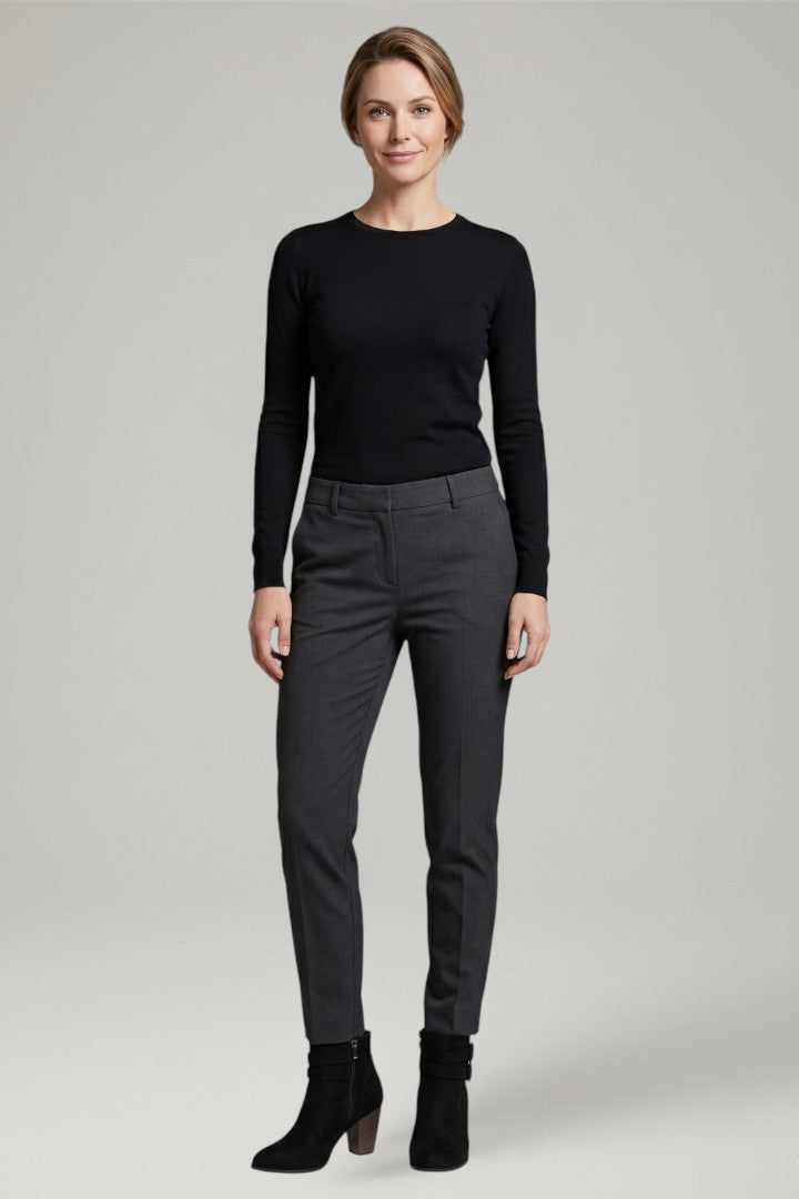 Woman wearing a black long-sleeve top and gray pants on a light gray background