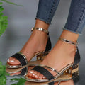 Black and gold high-heeled sandals worn with blue jeans on a neutral background