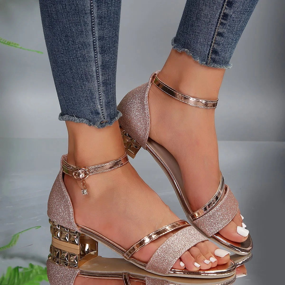 Rose gold glittery high-heeled sandals worn with blue jeans on a neutral background