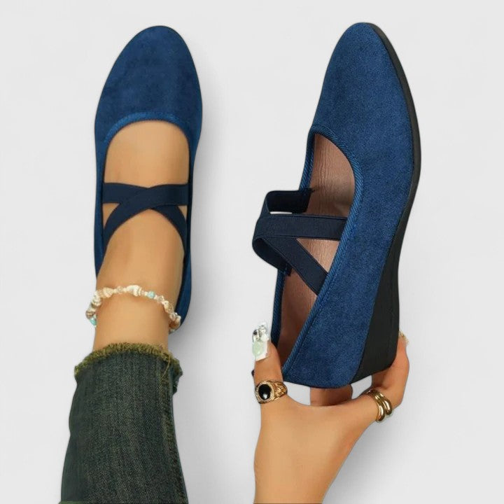Blue suede shoes with criss-cross straps worn by a person on a light gray background