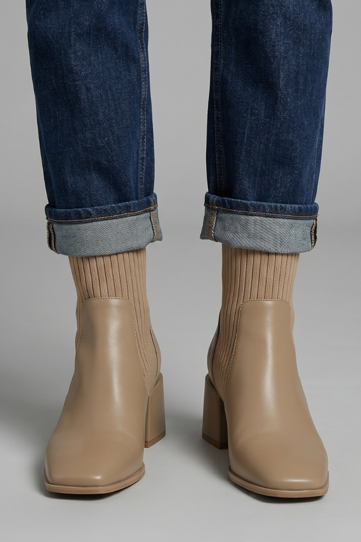 Beige ankle boots worn with rolled-up jeans on a neutral background