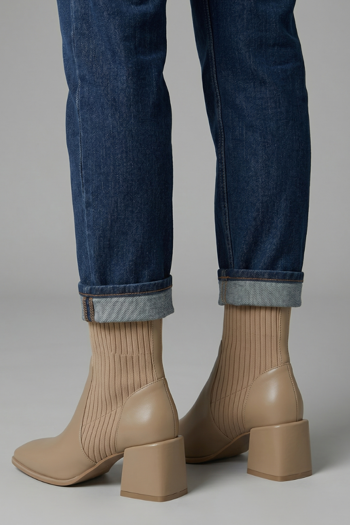 Beige ankle boots worn with rolled-up blue jeans on a neutral background