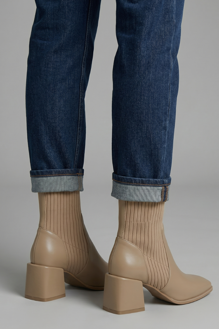 Beige ankle boots worn with rolled-up blue jeans on a neutral background