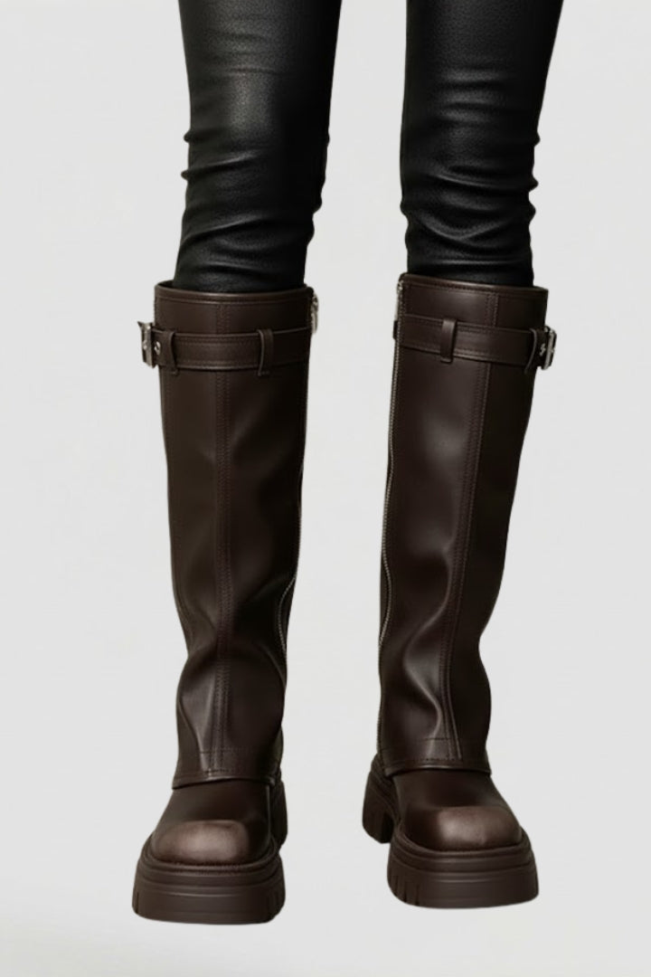 Brown knee-high boots worn with black pants on a light gray background