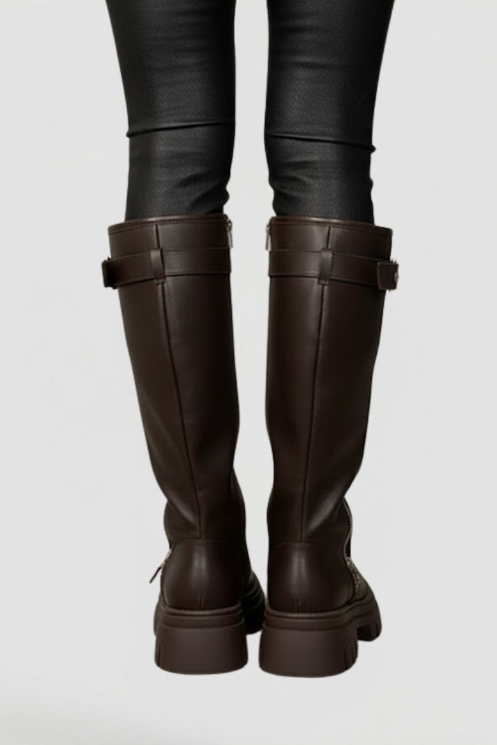 Brown knee-high boots worn with black leggings on a light gray background