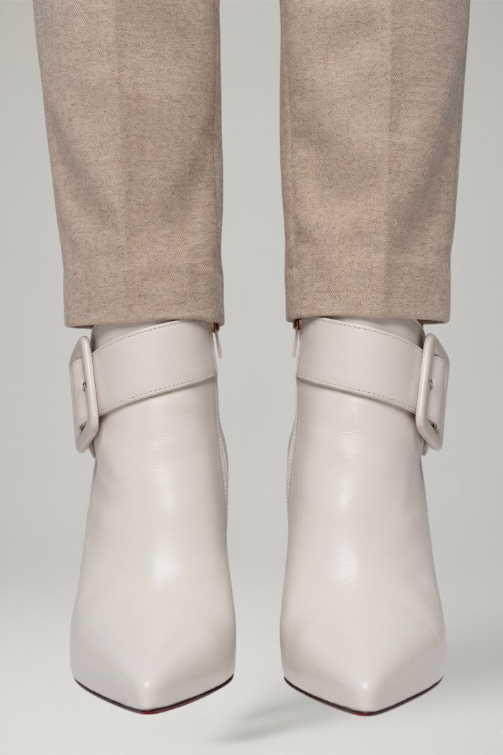 White ankle boots with buckles worn with beige pants on a light gray background