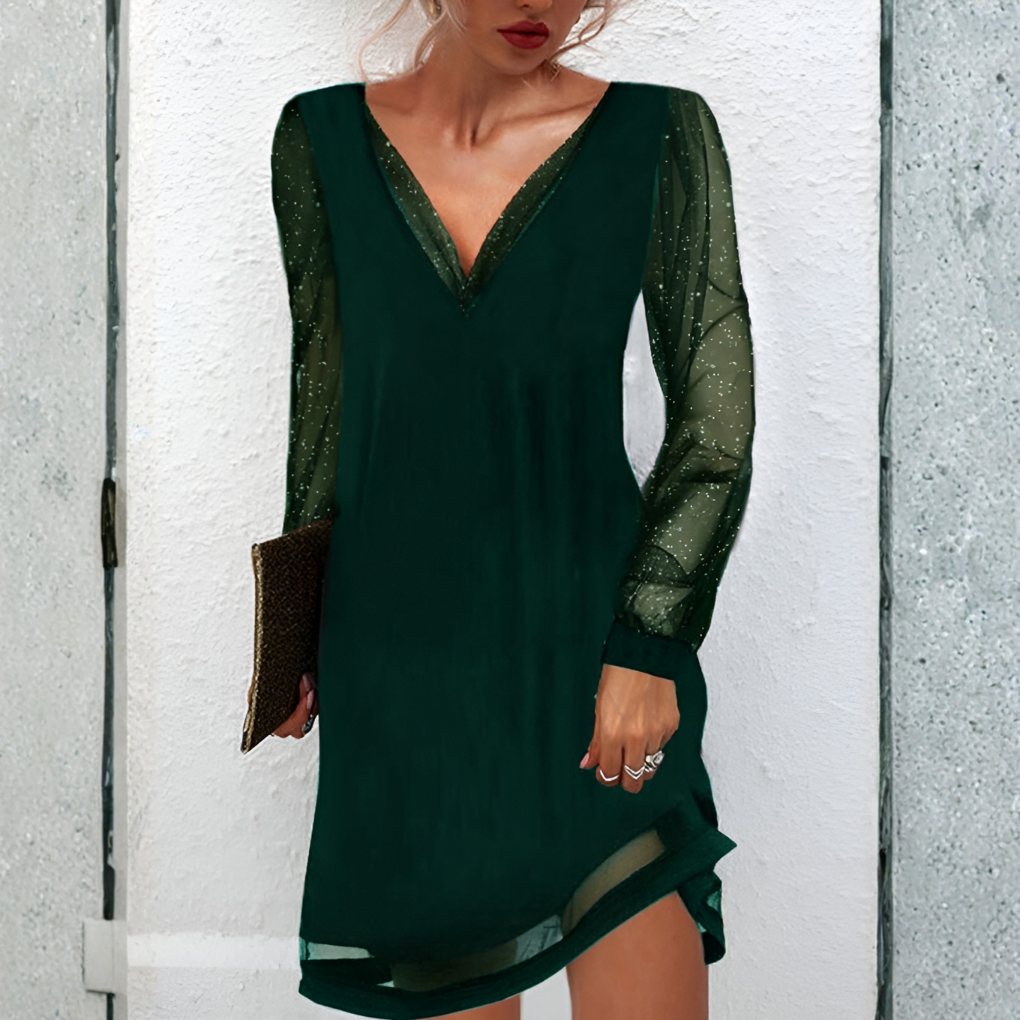 Green dress with sheer sleeves worn by a person against a white wall.