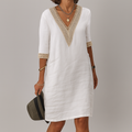 Woman wearing a white dress with gold accents against a gray background