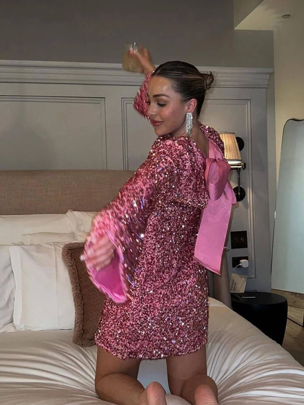 Woman in a pink sequin dress posing in a bedroom.