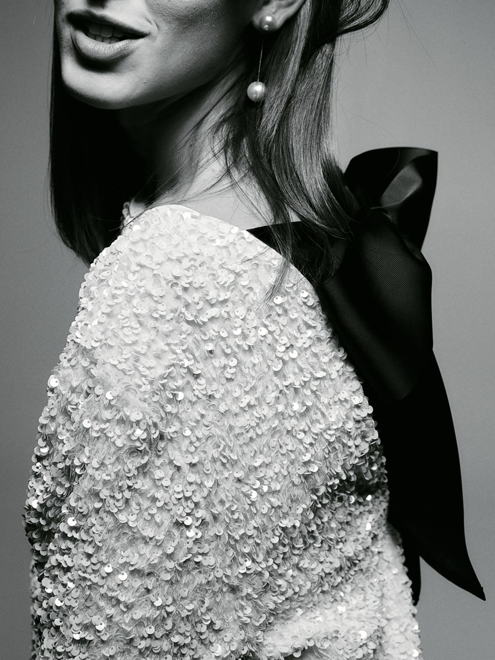 Close-up of a person wearing a sequined garment with a black bow on a gray background