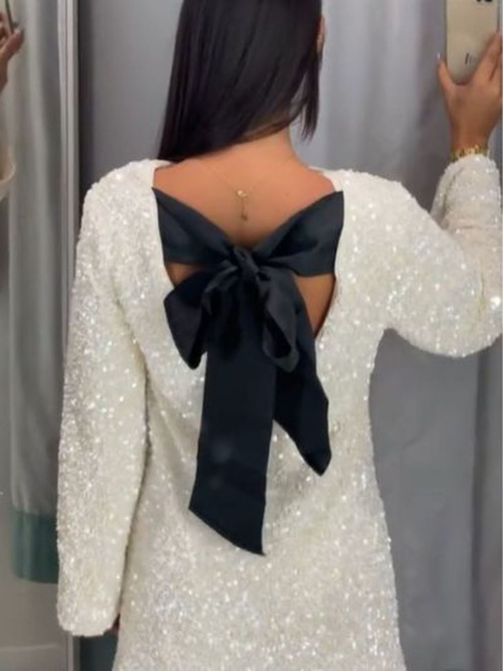 White dress with a black bow at the back worn by a person, against a neutral background.