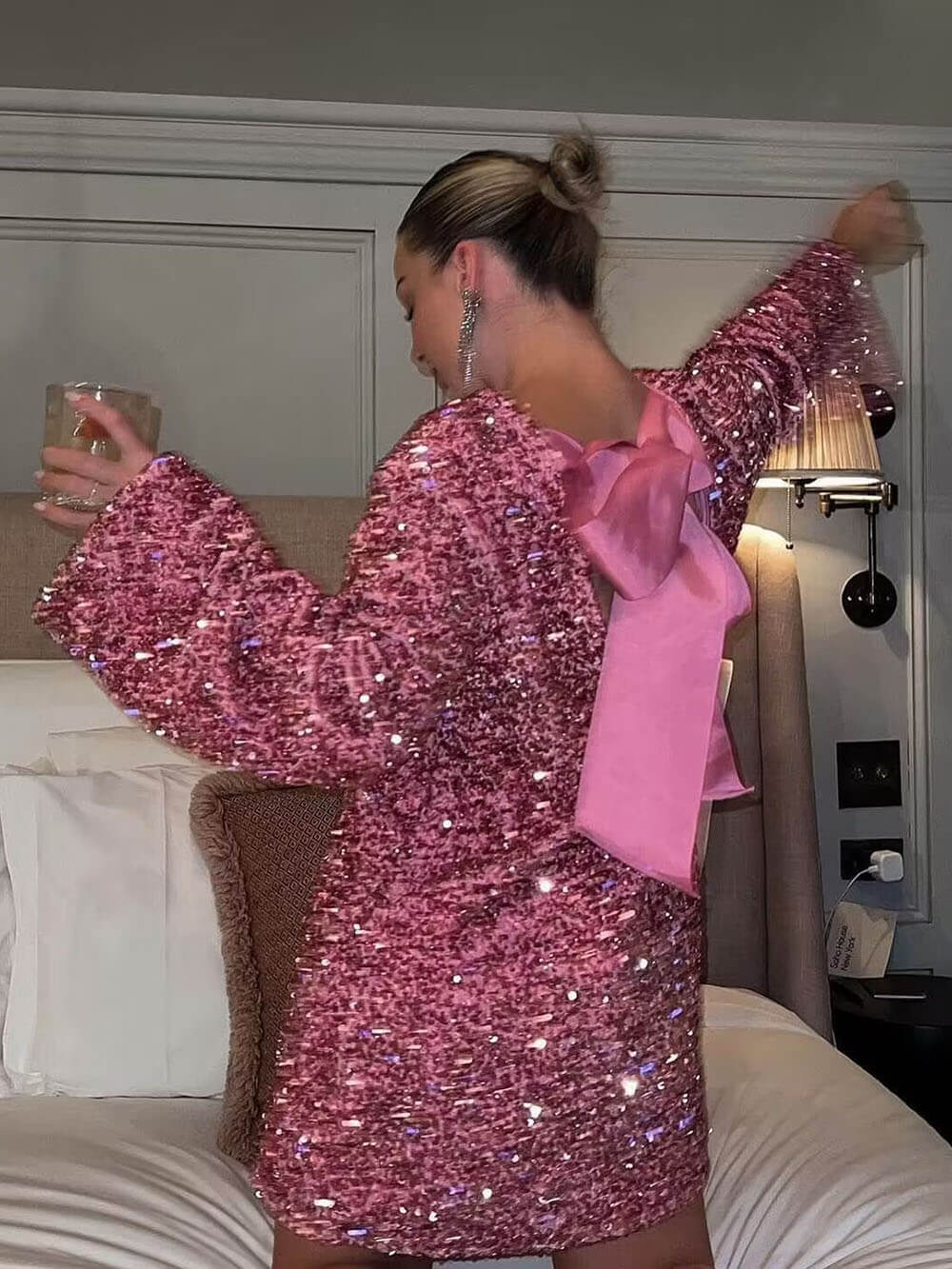 Person wearing a pink sequin dress with a large bow in a room.